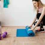 Crop fit sportswoman unfolding fitness mat on floor