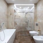 Interior of contemporary bathroom with marble walls and comfortable shower cabin under bright light of lamp