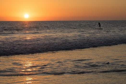 Silhouette of a Person Paddleboarding near the Coast at Sunset