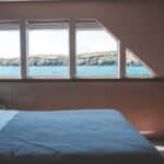 Interior of cabin in modern yacht with comfortable bed and windows overlooking picturesque sea and rocky cliff on sunny day