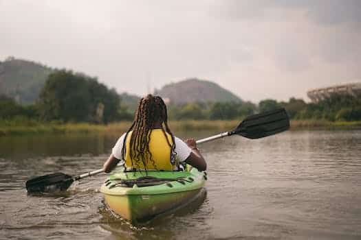 Person in Yellow Life Jacket Sitting on Green Kayak on River