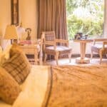 Comfortable sunny hotel room with soft bed and classic armchairs placed near big window aside white vanity table