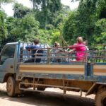 Travelers sitting in truck driving on dusty road in lush forest while exploring nature during vacation