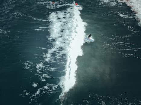 Drone view of surfers riding on surfing boats in wavy sea on sunny day
