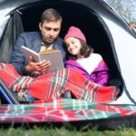 Father and Daughter Reading a Book while Sitting Inside the Tent
