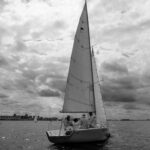 Grayscale Photo of Sail Boat on Sea Shore