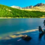 Scenic View Of The Mountains With Green Pine Trees Beside Calm Body of Water