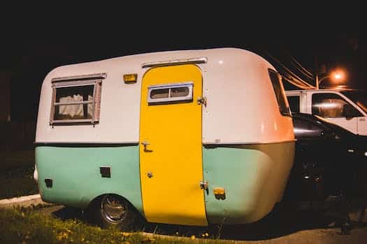 Small cozy retro camping trailer with yellow door placed on parking on street at night time