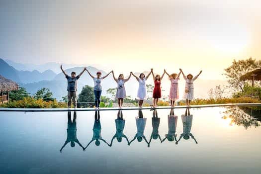 Group of happy people in colorful summer clothes raising hands and enjoying nature spending holidays together