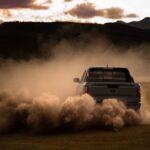 A truck driving through the dust on a field